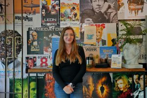 Pamela Dzi&oacute;bek &ndash; właścicielka kawiarni Może Kawy? na tle ściany z plakatami filmowymi 