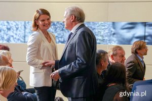 Kobieta i mężczyzna witają się na sali pełnej ludzi.