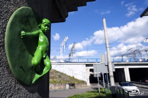 Zielona rzeźba małego dziecka na filarze kładki dla pieszych.