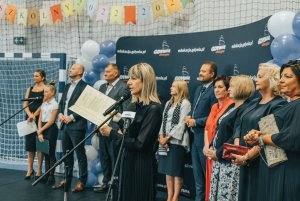 Na pierwszym planie mikrofony, przemawiająca pani dyrektor, w tle przedstawiciele władz