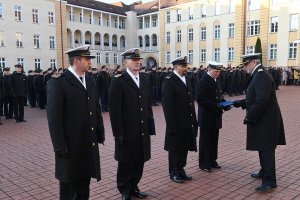 Oficer Marynarki Wojennej wręcza nominacje czterem żołnierzom Marynarki Wojennej w mundurach.