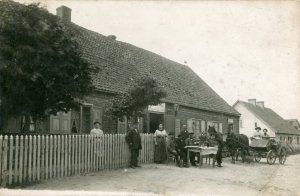 Stara pocztówka Gdyni. Wiejski dom murowany, przed nim ludzie przy stole i w powizie konnym.