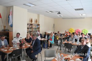 Liczna grupa osób siedzących przy stołach w udekorowanej sali