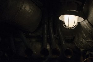 Ciemne wnętrze maszynowni okrętu rozświetla okrętowa lampa.
