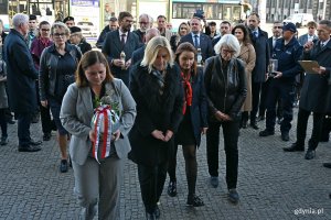 Delegacja gdyńskich samorządowc&oacute;w składająca znicz pod tablicą pamiątkową, kt&oacute;ra znajduje się na fasadzie Dworca PKP Gdynia Gł&oacute;wna, podczas uroczystości z okazji 87. rocznicy pierwszych wysiedleń Gdynian. Od lewej: radna Gdyni Agnieszka Tokarska, prezydent Gdyni Aleksandra Kosiorek, przewodnicząca Rady Miasta Gdyni Beata Zastawna oraz radne Gdyni Anna Szpajer i Joanna Zielińska