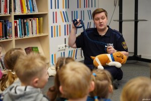 Kamil Zdunek z Wydziału Straży Miejskiej i Zarządzania Kryzysowego Urzędu Miasta Gdyni pokazuje dzieciom na pluszowym psie zakładanie smyczy