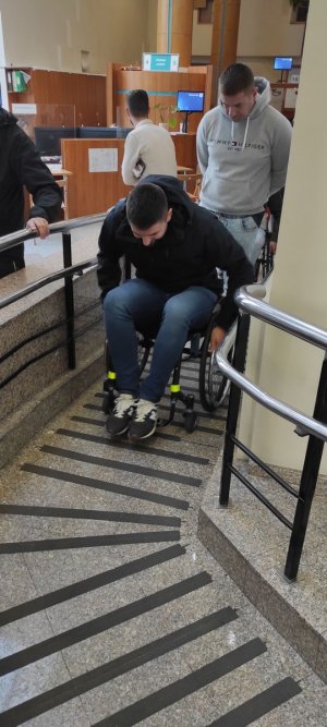 Policjant na wózku inwalidzkim próbuje poruszać się po budynku urzędu