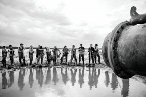 Czarno-biała fotografia przedstawiająca szereg mężczyzn z łopatami stojący przy dole wypełnionym wodą