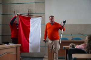 Mężczyzna w pomarańczowym swetrze pokazuje biało-czerwoną flagę