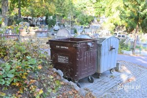 Brązowy i srebrny pojemnik na śmieci ustawione na chodniku obok porośniętego krzewami wzniesienia na cmentarzu