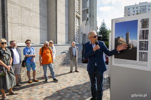 Ludzie oglądają wystawę przed kościołem, o której opowiada jeden mężczyzna.