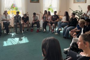 Przedstawiciele Młodzieżowej Rady Miasta Gdyni oraz młodzieży z Gruzji. Kilkanaście osób w różnym wieku, kobiety i mężczyźni. Siedzą w okręgu na fotelach, w sali wizytowej podczas spotkania i rozmowy. 