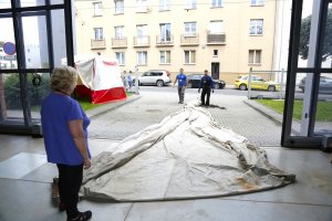 Na pierwszym planie kobieta w niebieskiej bluzce stoi przy rozłożonym na podłodzie i chodniku żaglu z „Daru Pomorza”. W oddali dwaj pracownicy Centrum Konserwacji Wraków Statków rozwijają żagiel //  fot. materiały prasowe Narodowego Muzeum Morskiego 