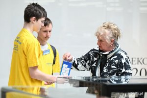 Starsza pani wrzuca pieniądze do skarbonki dw&oacute;ch młodych wolontariuszy w ż&oacute;łtych koszulkach