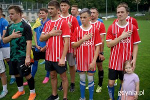 Piłkarze śpiewają hymn trzymając rękę na piersi.