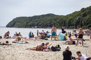 Ludzie na plaży, w tle zarośnięte lasem wzgórza.