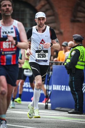 Mężczyzna w czarno-białym stroju sportowym biegnący po ulicach miasta w otoczeniu innych biegaczy