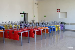 Pomieszczenie ze stołami i krzesłami ułożonymi na wierzchu, podłoga przygotowana do mycia 