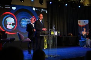 Przemysław Sztandera, prezes Pomorskiej Specjalnej Strefy Ekonomicznej (z przodu, przy mikrofonie) oraz Maciej Kazienko, wiceprezes Pomorskiej Specjalnej Strefy Ekonomicznej (z tyłu) podczas gali z okazji 25-lecia Pomorskiej Specjalnej Strefy Ekonomicznej// fot. materiały prasowe PSSE