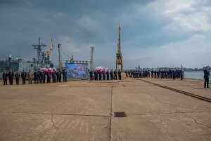 Uroczystość podpisania umowy na zakup nowych okrętów dla Marynarki Wojennej w PGZ Stoczni Wojennej. Po prawej przy mikrofonie - Mariusz Błaszczak, minister obrony narodowej. Na nabrzeżu stoją marynarze i goście uroczystości. W tle okręty i stoczniowy dźwig // fot. bsmt Michał Pietrzak 