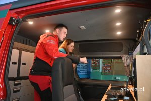 Ratownik medyczny i elegancko ubrana kobieta stojący w szarym wnętrzu furgonu