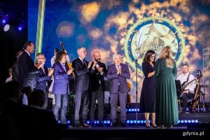 Agnieszka Jankowiak-Maik ( w zielonej sukience) odbiera medal z rąk prezydent Gdańska Aleksandry Dulkiewicz i innych samorządowców (od lewej): Mieczysława Struka - marszałka województwa pomorskiego, Wojciecha Szczurka - prezydenta Gdyni, Arkadiusza Klimowicza - burmistrza Darłowa, Jacka Karnowskiego - prezydenta Sopotu, Jacka Jaśkowiaka - prezydenta Poznania, Jacka Sutryka - prezydenta Wrocławia oraz Tadeusza Truskolaskiego - prezydenta Białegostoku // fot. Karol Stańczak