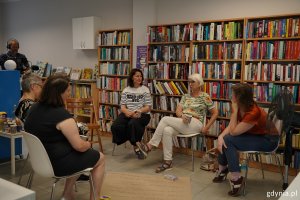 Uczestnicy spotkania w Bibliotece Działki Leśne siedzą pod regałami z książkami