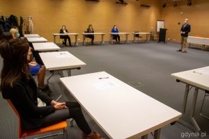 Nauczyciele siedzą za stołami z zachowaniem dystansu.