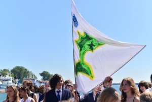 Grupa uczniów z żaglem na tle nieba. Na żaglu zielona ryba