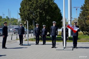 Poczet flagowy i przedstawiciele student&oacute;w podczas podniesienia bandery na maszt na uroczystym apelu z okazji otwarcia sezonu żeglarskiego w Ośrodku Żeglarstwa i Sport&oacute;w Wodnych Uniwersytetu Morskiego