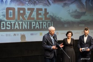 Gdyńska premiera filmu „Orzeł. Ostatni patrol”. W sali kinowej Gdyńskiego Centrum Filmowego przy mikrofonie stoi Leszek Kopeć i prowadzący uroczystość