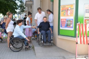 Kobieta na wózku inwalidzkim instruuje mężczyznę na wózku jak zjeżdżać z podjazdu dla wózków przed sklepem.