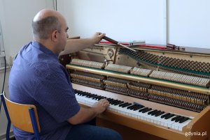 Mężczyzna siedzący na krześle, twarzą do pianina, w rękach trzyma narzędzia do strojenia pianina