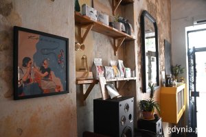 Wnętrze kawiarni „Kosmos”: półki z kawą i sierpniowa grafika Pawła Smardzewskiego