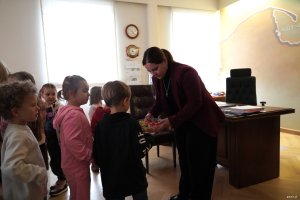 Kobieta w bordowej marynarce częstuje dzieci cukierkami