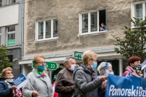 Wielobarwny Pomorski Przemarsz Seniorów ulicami Gdyni. W oknie kamienicy obserwujący ludzie. Fot. Karol Stańczak