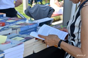 Kobieta w sukience w biało-czarne pasy przy jednym ze stoisk podczas Pleneru Literackiego w Gdyni. W ręku trzyma otwartą książkę // fot. Magdalena Czernek