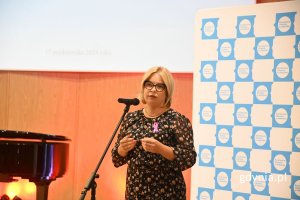 Kobieta elegancko ubrana stoi na scenie przed mikrofonem