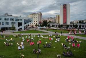 Różnokolorowe leżaki są rozstawione na trawie na placu Grunwaldzkim. W tle budynek Gdyńskiego Centrum Filmowego i hotelu Mercure, na którym jest rozwieszony czerwono-czarny baner Nagrody Literackiej GDYNIA // fot. Anna Rezulak