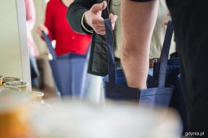 Pakowanie wielkanocnych paczek dla potrzebujących, które odbyło się w Centrum Aktywności Seniora. Na zdjęciu widać ręce wolontariuszy, którzy trzymają siatki. Inni wkładają do nich produkty // fot. Kamil Złoch
