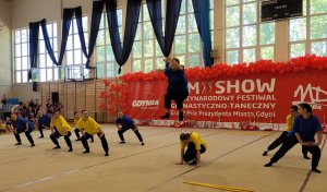 Tańcząca grupa młodych dziewcząt i chłopców, jeden z chłopców został na fotografii uwieczniony podczas podskoku