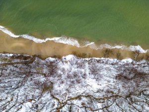 Widok z lotu ptaka przedstawiający plażę sąsiadującą z ośnieżonym lasem