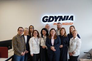 Obsługa punktu przy ul. Unruga 39 w towarzystwie prezydent Aleksandry Kosiorek, wiceprezydentki Oktawii Gorzeńskiej, radnego miasta Łukasza Strzałkowskiego oraz radnych dzielnicy Obłuże: Macieja Dobbka, Izabeli Procelli-Szynwelskiej i Marka Urbaniaka na tle napisu: Gdynia moje miasto