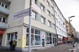 Tablica pamiątkowa została zamontowana na bocznej fasadzie kamienicy na rogu ulic Świętojańskiej i Derdowskiego. Na pierwszym planie drogowskaz z nazwami ulic. W tle budynek oraz mężczyźni montujący tablicę // fot. Sławomir Okoń
