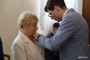 Mężczyzna w garniuturze przypina medal starszej pani w białej marynarce