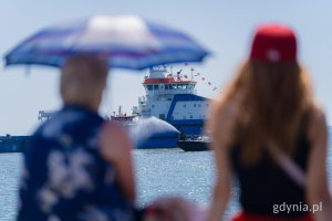 Wąski kadr, dwie kobiety oglądające ł&oacute;dź na morzu, jedna z nich trzyma parasolkę