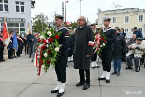 Andrzej Krajniak – członek zarządu stowarzyszenia Gdynian Wysiedlonych składa kwiaty przed pomnikiem Gdynian Wysiedlonych podczas uroczystości upamiętniających 84. rocznicę wysiedlenia ludności polskiej z Gdyni . Przed nim i za nim marynarze z wieńcami w rękach
