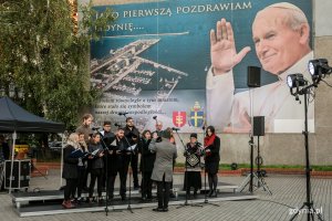 Występ chóru z okazji obchodów Dnia Papieskiego w Gdyni. Artyści stoją przy bazylice mniejszej w Gdyni na tle baneru z Janem Pawłem II // fot. Karol Stańczak