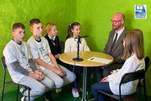 Grupa osób siedząca przy okragłym stole podczar nagrania video-wywaidu, w tle greenbox