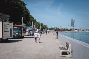 Foodtrucki, bulwar oraz morze. W oddali: drzewa i miejska zabudowa.